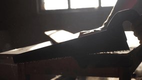 man carpenter handmade and craft concept slow motion video. carpenter sawing a tree in a workshop sawing sunlight from a window silhouette. woodworker engaged in processing wood at the sawmill