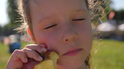 Little kid girl on nature picnic eat bite an apple enjoying delicious fruit