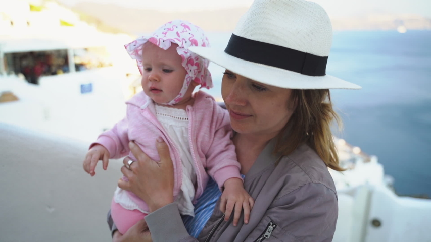 Mom holds her daughter in her arms and looks at her. Against the backdrop of the sunset.