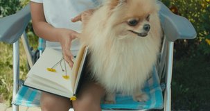 Little pretty girl sitting in chair, looking notebook with herbarium. Sunny day, summer house. Interesting hobby. Funny dog playing with kid. 4k raw slow motion footage video 60 fps