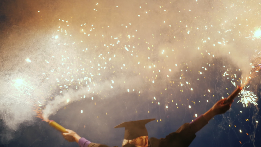 A joyful graduate in a mantle and cap waving two fireworks. Graduation party Royalty-Free Stock Footage #1035049925