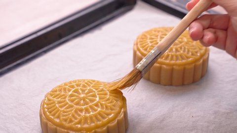 Process of making moon cake for Mid-Autumn Festival - Woman brushing egg liquid on pastry surface before baking. Festive homemade concept, close up.