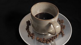 Morning hot coffee cup rotating on display with coffee beans around it. Ideal for videos related with cafes, cafeterias, coffee shops, documentaries, organic coffee, flavours of the world, health, etc