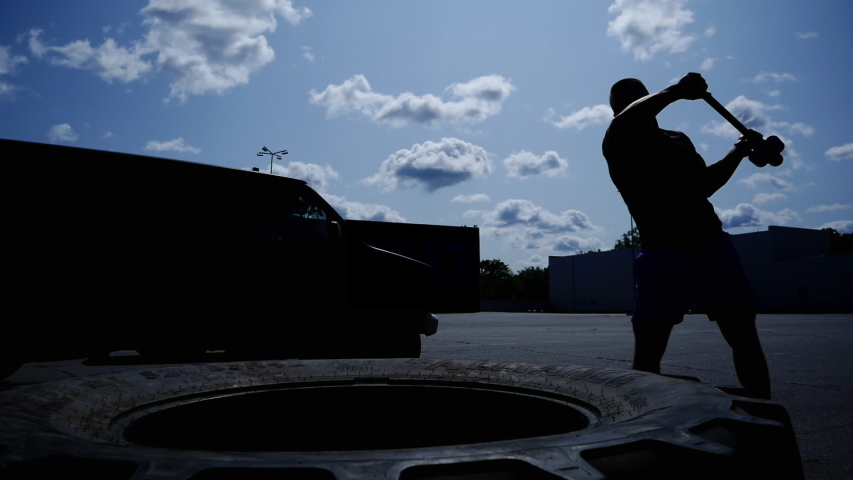 Silhouette of sports muscular fitness man hits the tire with a hammer in close-up, throws a hammer, concept of motivation and sport