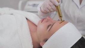 Side view of attractive brunette girl with clear skin doing facial cosmetic procedures while lying on coach at modern beauty salon. Young lady with natural beauty receiving professional treatment