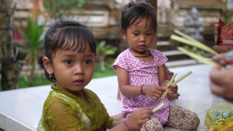 Young children in Bali help mom make Hindu offerings as part of their chores. Kids learning to work at young age. Asian, Indonesian, culture and religion. Video stock