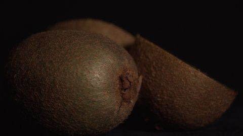 Super close up of whole and sliced kiwifruit rotating on black background. Static. Eye level