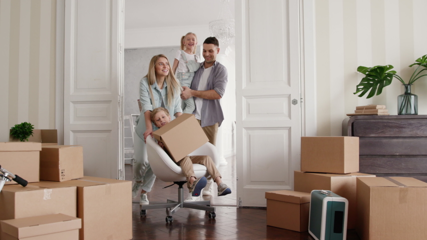 Active Homeowners Move in Rental Large Flat. Smile of Small Child Riding a Chair. Carton Packaging of Positive Relocating. Laughing Mom and Caucasian Dad Enjoy Life. Cute Emotion of Two Little Babies Royalty-Free Stock Footage #1035079478