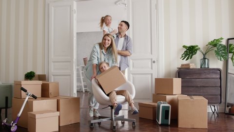 Active Homeowners Move in Rental Large Flat. Smile of Small Child Riding a Chair. Carton Packaging of Positive Relocating. Laughing Mom and Caucasian Dad Enjoy Life. Cute Emotion of Two Little Babies