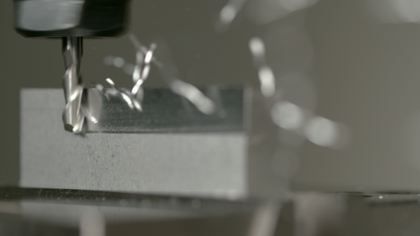 SLOW MOTION, MACRO, DOF: Twisted pieces of excess metal fly off a piece of aluminium during lathing by a CNC drill. Fine cut end mill shaving the side of a matt block of metal. Micro machining process Royalty-Free Stock Footage #1035090152