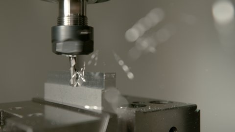 SLOW MOTION, MACRO, DOF: Shiny chips of metal come flying off a workpiece during end milling. Sharp cutter spinning and shaving the side of a matt block of aluminium. Conventional metalwork method.