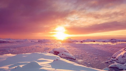 Antarctica sunrise behind glaciers silhouettes reflecting on frozen water under orange sky. Eploring beauty world. Travel, holidays, sports and recreation background. Slow motion 4K footage