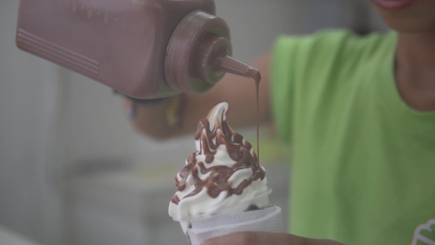 Pouring chocolate syrup on vanilla ice cream cone in slow motion