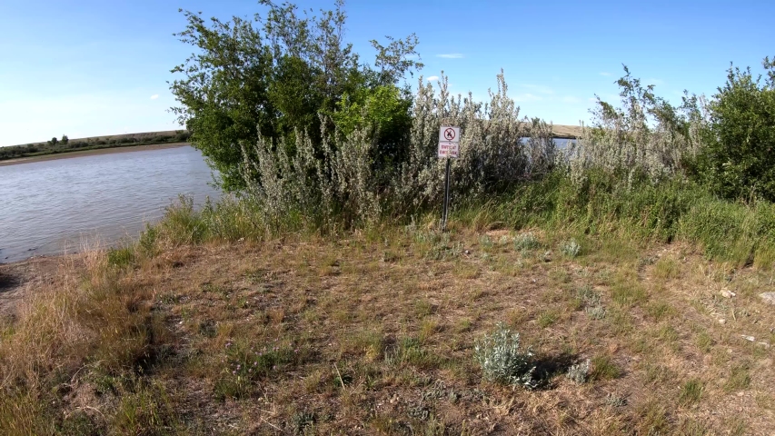 Walking up to a danger sign that reads ( Swim at your own risk ) next to a river in the country. ( 4k footage )