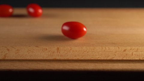 The cook cuts a ripe cherry tomato into two halves on a wooden surface