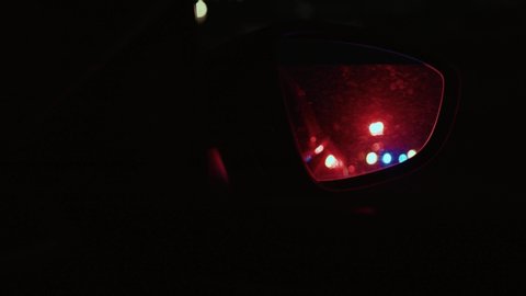 Side rear mirror view of police car chasing the driver pulling him over behind on the highway at night. Police emergency call. Raid.