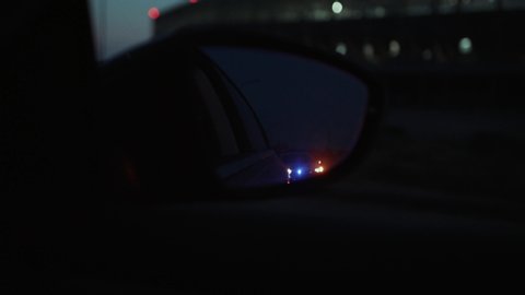 Traffic police arrest the driver. Car rear mirror view of police car approaching and stopping on the road at night. Police on duty.