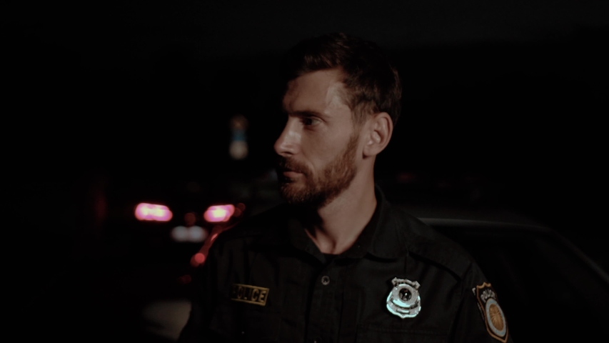 Portrait of cheerful handsome policeman smiling broadly against his patrol car at night. Police officers on durty in the city. Royalty-Free Stock Footage #1035106469