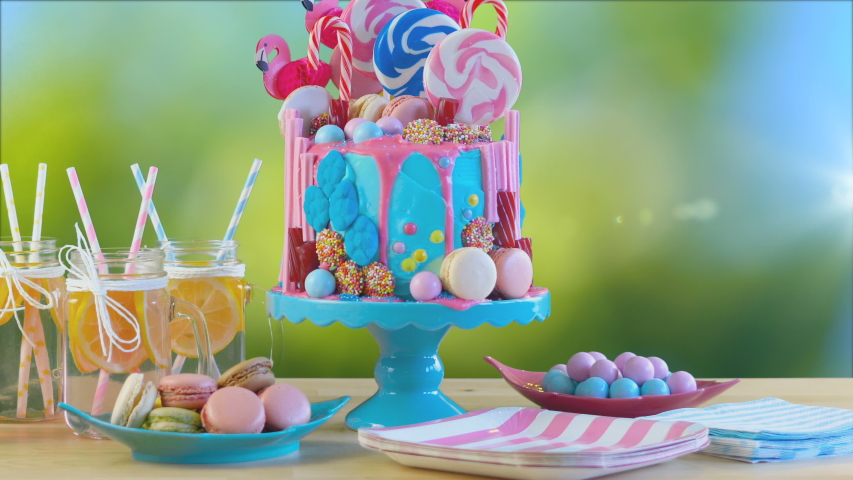 On-trend candyland fantasy drip cake with pink lemonade in garden party setting with lens flare.