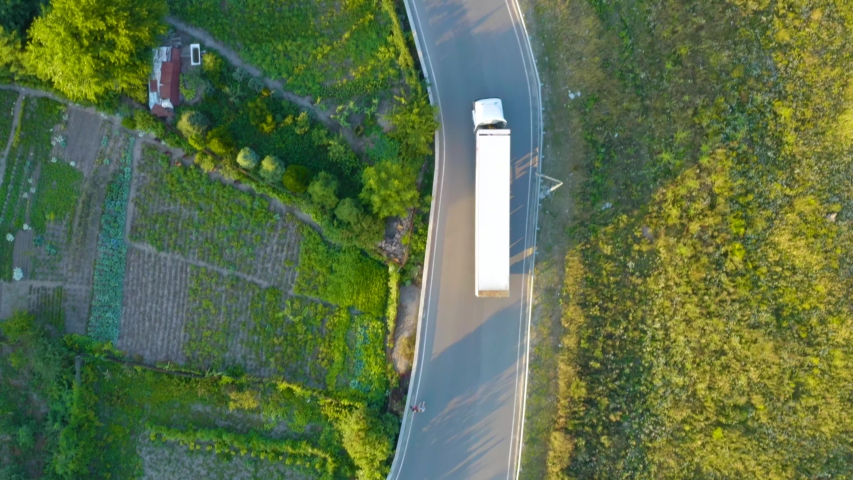Aerial following shot of a semi-trailer truck travelling on a country road on a summer sunset