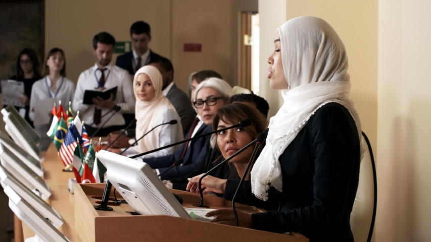 Muslim woman in hijab talking to audience at rostrum, smiling and walking away while multiethnic participants applauding her speech at press conference Royalty-Free Stock Footage #1035115805
