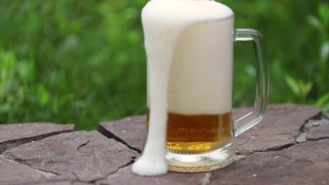 Beer. A mug is placed on a stone surface and beer is poured into it. Foam pours over the edge of the mug.