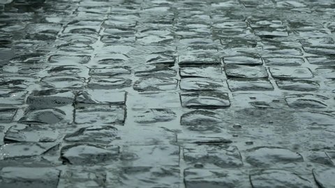 Rain falling and pooling on a cobblestone side walk or street