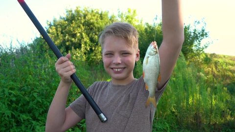 Portrait of happy proud kid holding fish just caught in lake. 