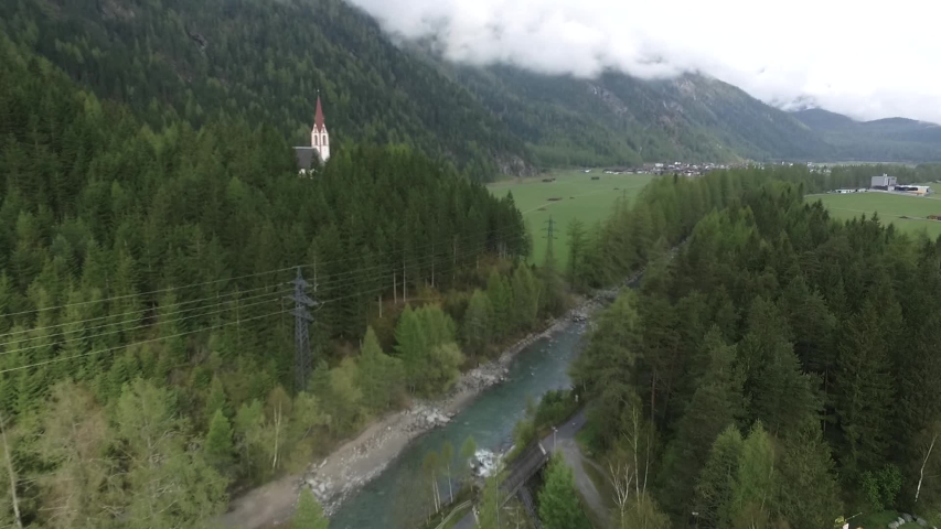 A drone shot of a church near a river by the alpes