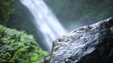 Slow motion panning up shot in front of a gushing NungNung Waterfall in Bali, Indonesia following a rain storm.