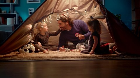 Dad with daughters in a tent at home. Dad imitates a owl.