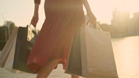 Woman in red dress with shopping bags walking in a city at sunset. Slow motion