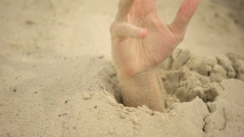 Male hand sinking in puddle of quicksand, dangerous travels in desert, closeup