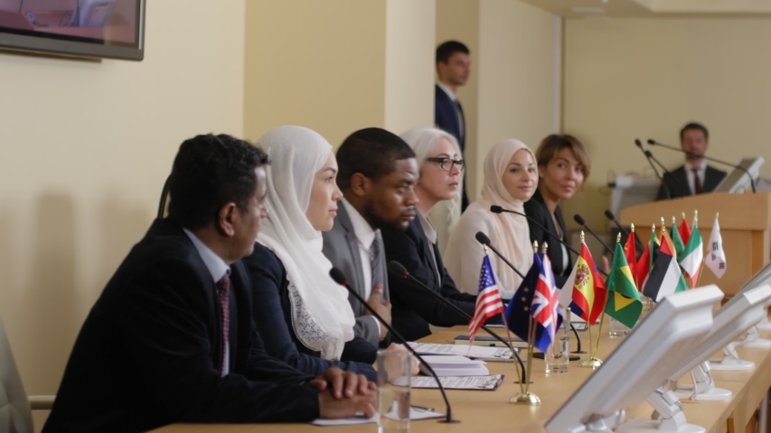 Multiethnic participants standing up and nodding head to audience while being introduced in the beginning on political press conference