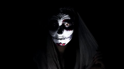 Halloween mask CALAVERA CATRINA. A girl in a blinking and frightening light. Mexican day of the dead. Portrait of a young woman with scary multi-colored makeup for Halloween on a dark background. 4K