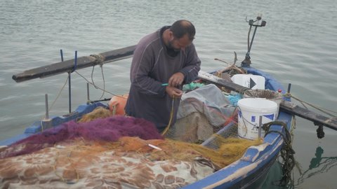 Mytilene / Greece - 05 10 2019: Greek fisherman manually fixing net by hands slow motion
