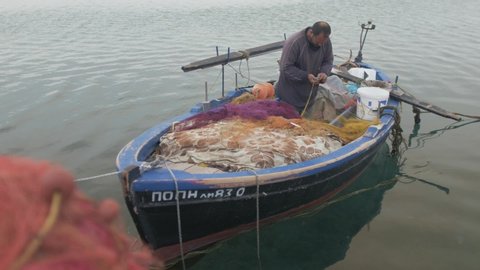 Mytilene / Greece - 05 10 2019: Fisherman repairing nets by hand in wooden fishing boat