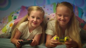 Kids playing video games at home. Children have fun together with joysticks in hands. Happy girls enjoy video game