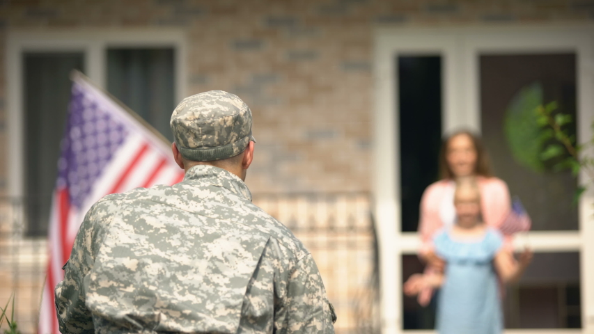 Daughter running to embrace father soldier, happy homecoming, holding US flag