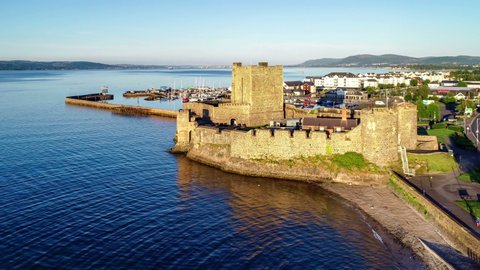 Medieval Norman Castle in Carrickfergus near Belfast in sunrise light. Aerial 4K flyby video with marina, yachts, parking, town and far view of Belfast in the background
