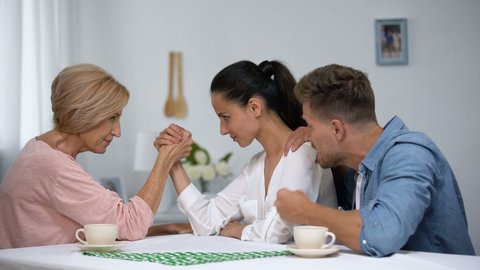 Man supporting wife during arm wrestling competition with mother, family battle
