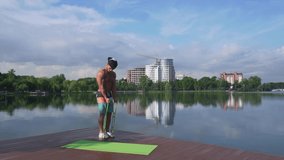 Muscular sportsman wearing cap, shorts and sneakers holding rubber expander with both arms, pulling it to himself with green nature around. Concept of body care and physical activity