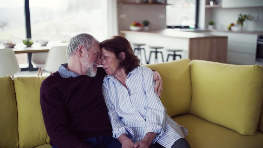 Affectionate senior couple in love sitting on sofa indoors at home, talking.