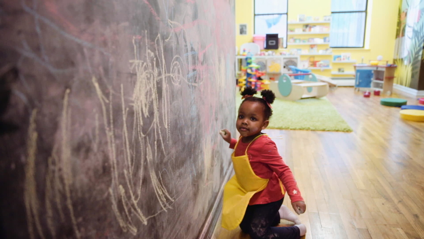 Black girl drawing on chalkboard wall at daycare | Shutterstock HD Video #1035169907