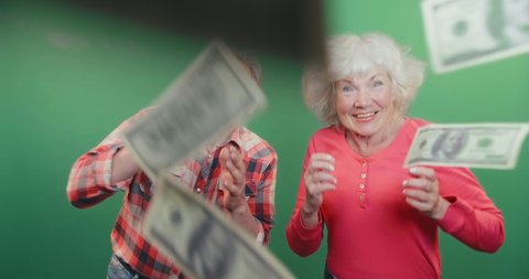Portrait of funny old couple happily dancing in money rain isolated on green background