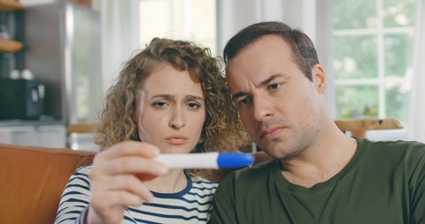 Close up of sad man and woman sitting together and looking at pregnancy test showing one line. Family financial difficulties