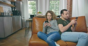 Man and young woman sitting on a couch and holding smartphones in their hands.