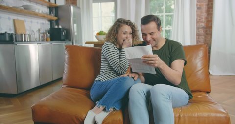 Excited amazed happy couple rejoicing reading good news holding mail paper letter celebrating taxes refund