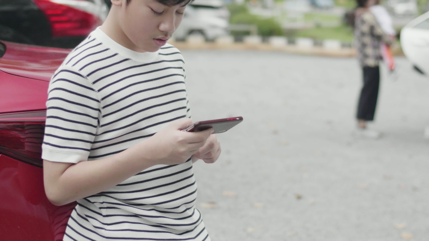 Asian preteen boy playing game on mobile near road with excite face.