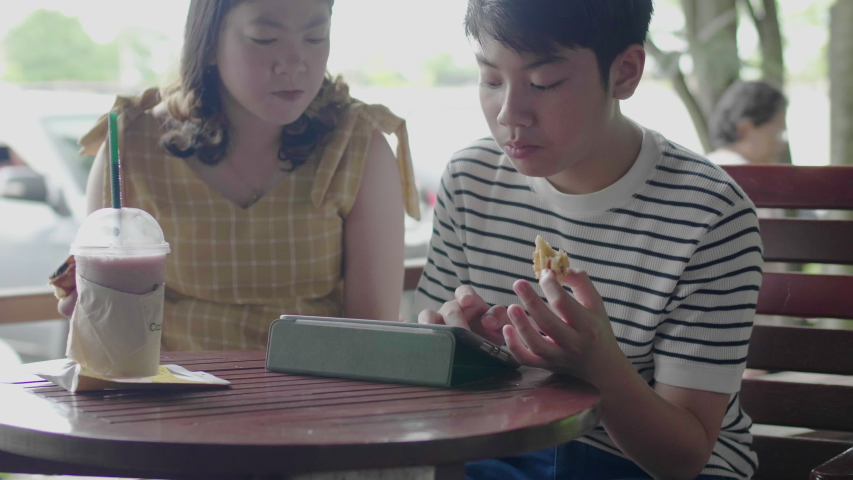 Asian boy with sister enjoy playing and eating on tablet computer with smile face.